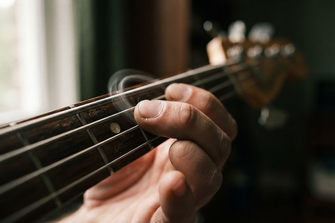 Close view of a musician’s fingers pressing a bass string against a fretboard